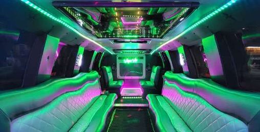Neon-lit stretch limousine interior with green and purple LED strips, quilted leather bench seating, mirrored ceiling and built-in screen — luxury party limo vibe