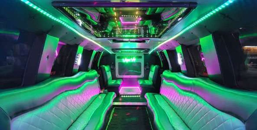 Neon-lit stretch limousine interior with green and purple LED strips, quilted leather bench seating, mirrored ceiling and built-in screen — luxury party limo vibe