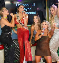 Bachelorette party karaoke with five women in sparkly outfits, a woman wearing a red sequin 'Bride to Be' sash singing into a microphone while friends cheer and pose in a colorful karaoke booth.