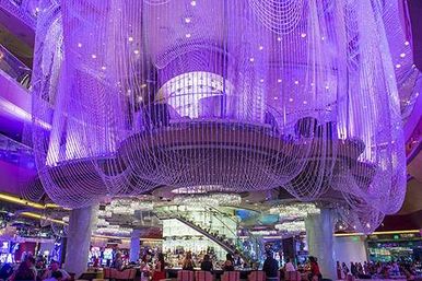 Giant purple-lit cascading chandelier installation over a lively casino atrium with central bar, escalator and gaming floor below