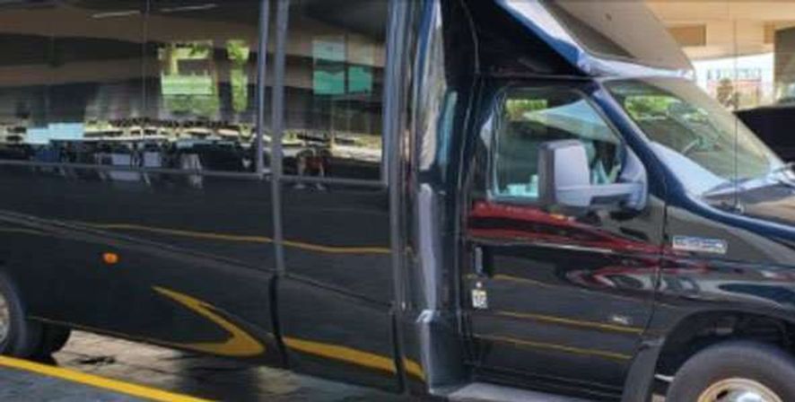 Sleek black airport shuttle van parked at a curbside with reflective windows, yellow curb markings and a sliding side door open for passenger pickup.