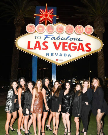 Group of women dressed for a night out posing under the illuminated Welcome to Fabulous Las Vegas Nevada sign on the Las Vegas Strip at night.