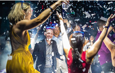 Adults dancing under falling confetti and colorful lights on a lively nightclub dance floor during a party celebration.