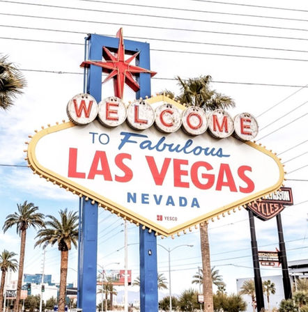 Iconic "Welcome to Fabulous Las Vegas Nevada" roadside sign with red star topper, palm trees, clear blue sky and distant Strip buildings