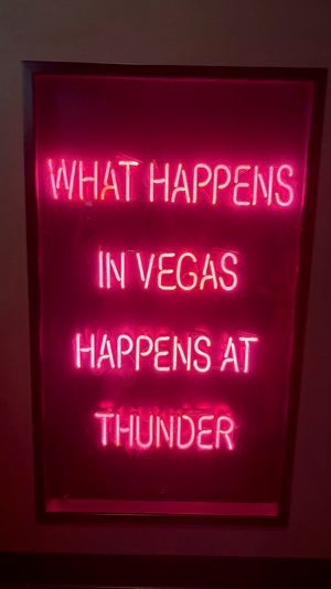 Vibrant pink neon sign reading WHAT HAPPENS IN VEGAS HAPPENS AT THUNDER, framed on a dark wall — neon Las Vegas wall art