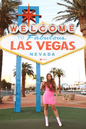 Woman in a pink mini dress and matching boots posing in front of the iconic Welcome to Fabulous Las Vegas Nevada sign with palm trees and warm sunset light