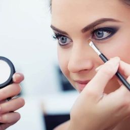 Close-up of a client in a beauty studio as a makeup artist applies concealer with a small brush to create a dramatic smoky eye look