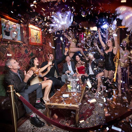 VIP nightclub party in an ornate lounge: friends cheering with cocktails as confetti falls and costumed dancers perform