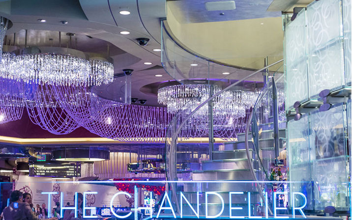 Glamorous casino-style lounge interior with cascading crystal chandeliers, purple mood lighting, a glass spiral staircase and neon-accented bar area