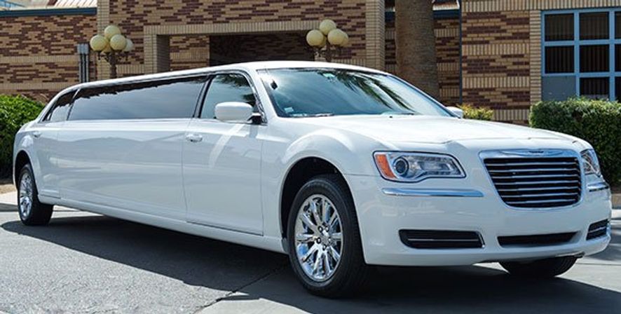 Gleaming white stretch limousine with chrome wheels and tinted windows parked by a brick building and palm tree — luxury wedding or event transportation.