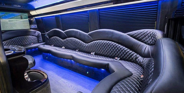Luxury limousine interior with curved black quilted leather seating, blue LED floor lighting, cup holders and wall-mounted screen