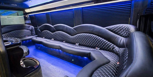 Luxury limousine interior with curved black quilted leather seating, blue LED floor lighting, cup holders and wall-mounted screen