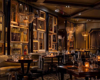 Luxurious dimly lit urban restaurant interior with velvet booths, wooden tables set with wine glasses and candles, gold-framed wall displays and crystal chandeliers.