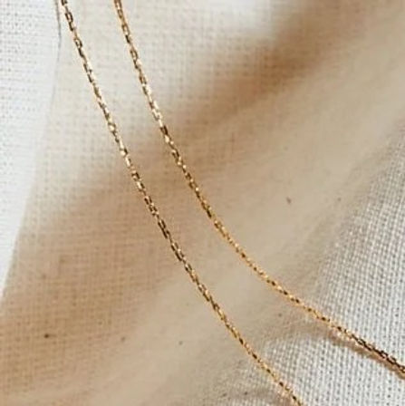 Delicate gold chains draped across textured beige linen fabric — minimal jewelry close-up product shot