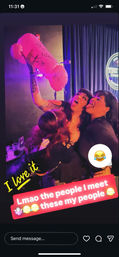 Three women at a neon-lit comedy club on a girls' night out, laughing and playfully posing with a large signed pink inflatable toy.
