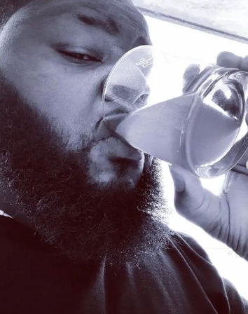 Close-up of a bearded man sipping from a tilted glass in a high-contrast black-and-white selfie