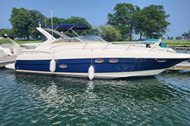 Sleek white-and-blue motor yacht docked at a marina on a sunny day, calm green water and tree-lined shoreline in the background.