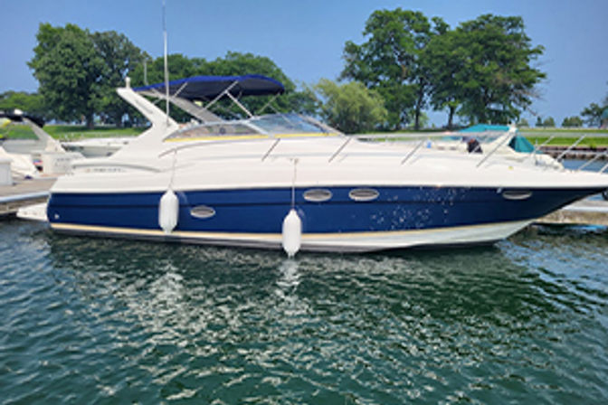 Sleek white-and-blue motor yacht docked at a marina on a sunny day, calm green water and tree-lined shoreline in the background.