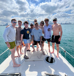 Nine friends smiling on the bow of a boat on Lake Michigan with the Chicago skyline under a partly cloudy summer sky