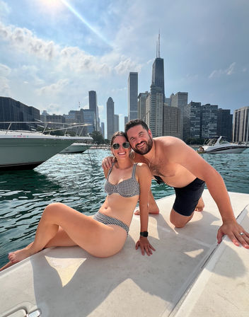 Smiling couple in swimwear relaxing on a boat with the Chicago skyline and skyscrapers over Lake Michigan on a sunny summer day