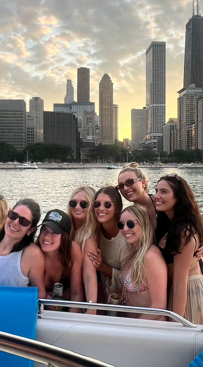Group of friends smiling on a boat at sunset on Lake Michigan with the Chicago skyline and skyscrapers in the background, colorful inflatable float and yachts on the water