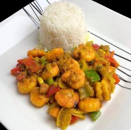Vibrant curried shrimp sauté with red and green bell peppers, served with a molded mound of steamed basmati rice on a white plate.