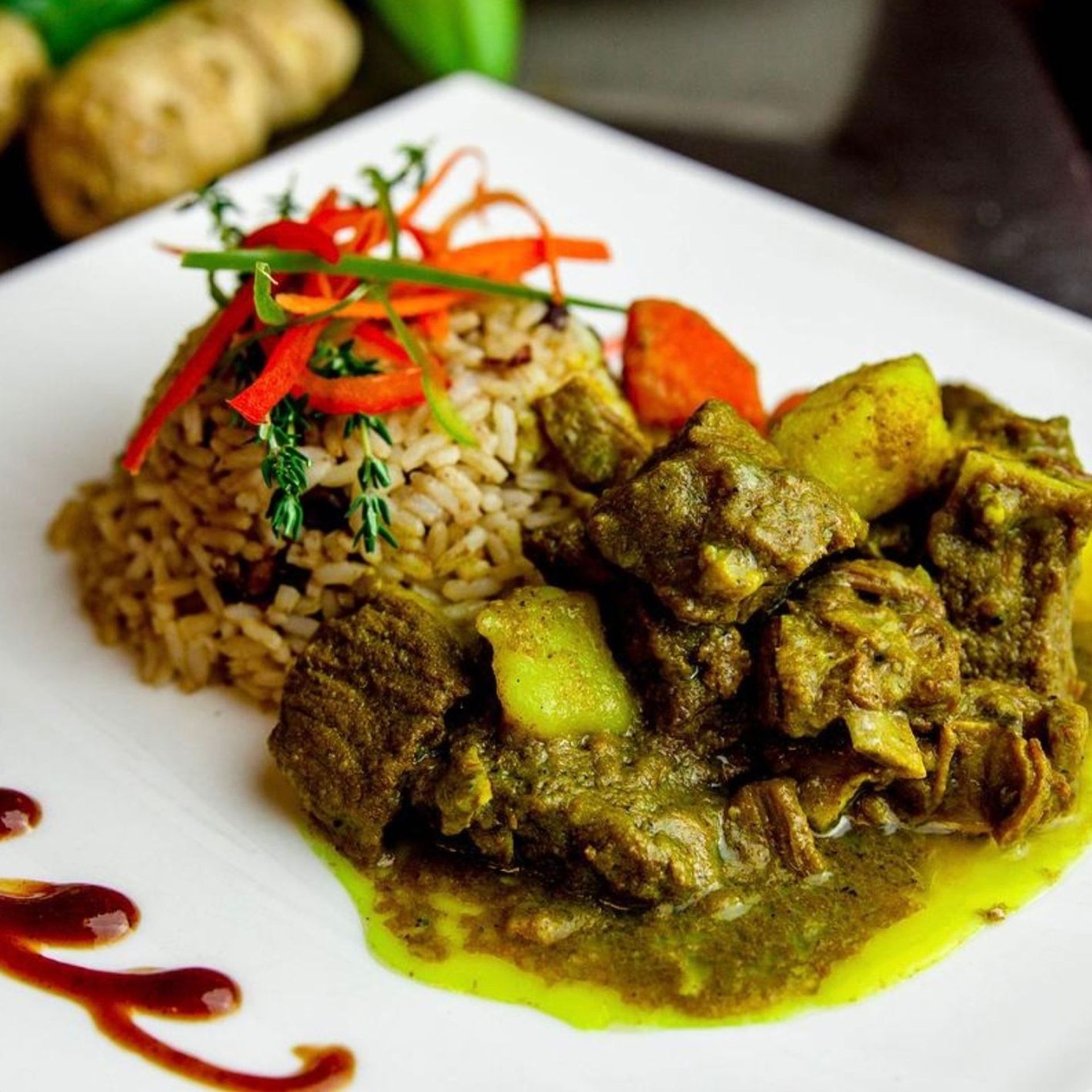 Hearty Jamaican curried goat with potatoes served beside seasoned rice, garnished with thyme and red pepper strips on a white plate