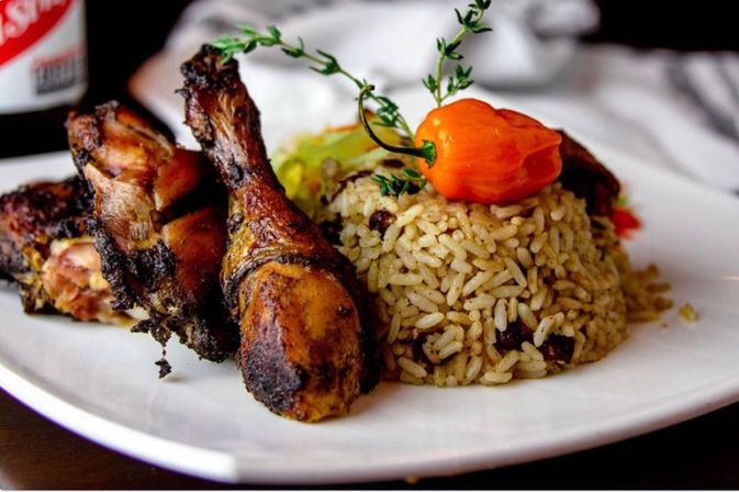 Caribbean-style jerk chicken drumsticks with seasoned rice and beans, topped with a fiery orange scotch bonnet pepper and thyme on a white plate.