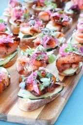Smoked salmon crostini on toasted baguette slices with cucumber, pickled red onion and microgreens arranged on a wooden serving board — colorful appetizer platter for brunch or catering.