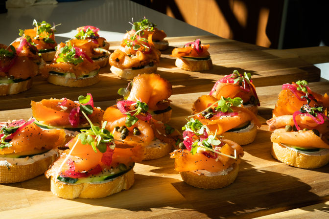 Gourmet smoked salmon crostini appetizer on toasted baguette slices with herbed cream cheese, cucumber, capers, pickled red onion and microgreens on a wooden serving board in warm natural light