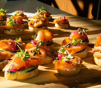 Gourmet smoked salmon crostini appetizer on toasted baguette slices with herbed cream cheese, cucumber, capers, pickled red onion and microgreens on a wooden serving board in warm natural light