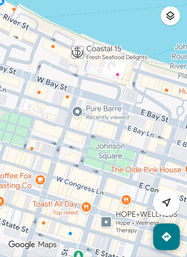 Stylized downtown waterfront map with a blue river at the top, grid of streets, a green park square, restaurant and coffee markers, and navigation icons