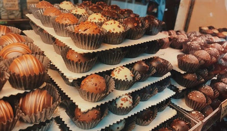 Close-up of stacked trays of assorted gourmet chocolate truffles—milk, dark and white varieties with drizzles and sprinkles, in paper cups in a shop display.
