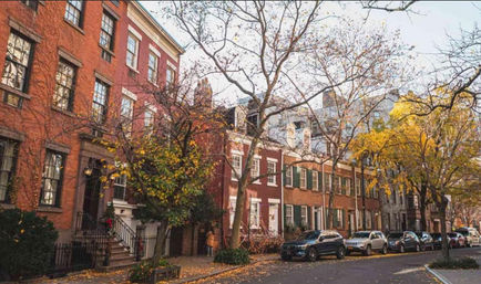 Cozy autumn streetscape of brick brownstone townhouses on a tree-lined urban street, stoops and parked cars with yellow leaves on the sidewalk