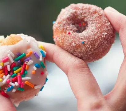 Close-up of two bite-sized mini donuts held in hand — one white-iced with rainbow sprinkles and one cinnamon-sugar coated