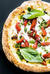 Close-up of gourmet Neapolitan-style pizza with blistered crust topped with creamy burrata, sliced strawberries, green pesto, pistachios and fresh basil