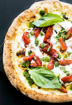 Close-up of gourmet Neapolitan-style pizza with blistered crust topped with creamy burrata, sliced strawberries, green pesto, pistachios and fresh basil