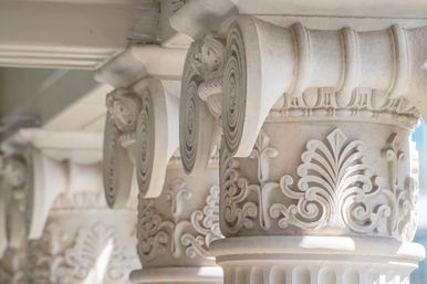 Close-up of sunlit classical stone column capitals with carved volutes and acanthus leaf motifs in a row, ornate architectural detail on a historic building facade