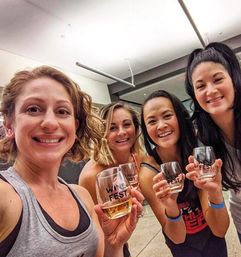 Group selfie of four smiling women indoors holding stemless glasses labeled "WINE FEST" at a wine festival tasting.