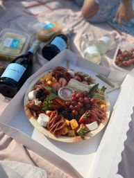Gourmet charcuterie board with grapes, strawberries, blackberries, cheeses, cured meats and crackers next to bottles of sparkling wine on a picnic blanket