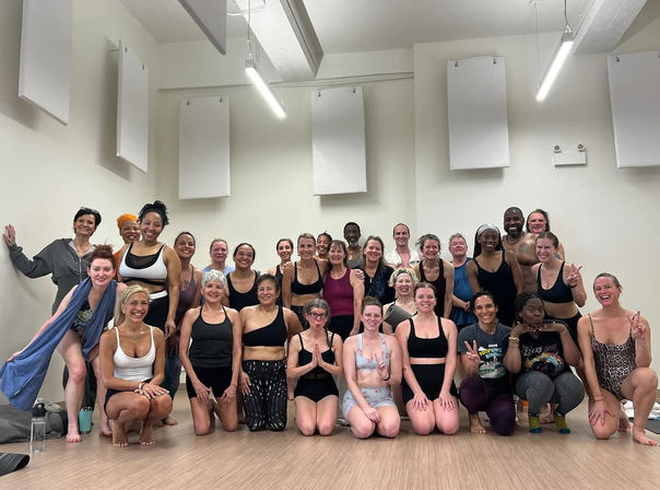 Smiling diverse adults in activewear posing barefoot on a wood floor after a group yoga class in an indoor studio with acoustic panels