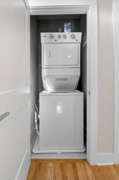 Compact stacked washer and dryer in a narrow home laundry closet with hardwood flooring and a box of dryer sheets on top — small apartment laundry nook.