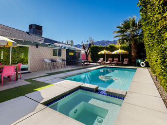 Sunny backyard pool with attached spa, striped yellow umbrellas, lounge chairs, palm tree and mountain backdrop