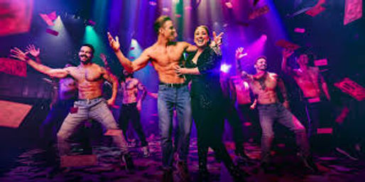 High-energy cabaret stage show with a smiling female lead surrounded by shirtless male dancers, flying paper bills and vivid purple-pink spotlights.