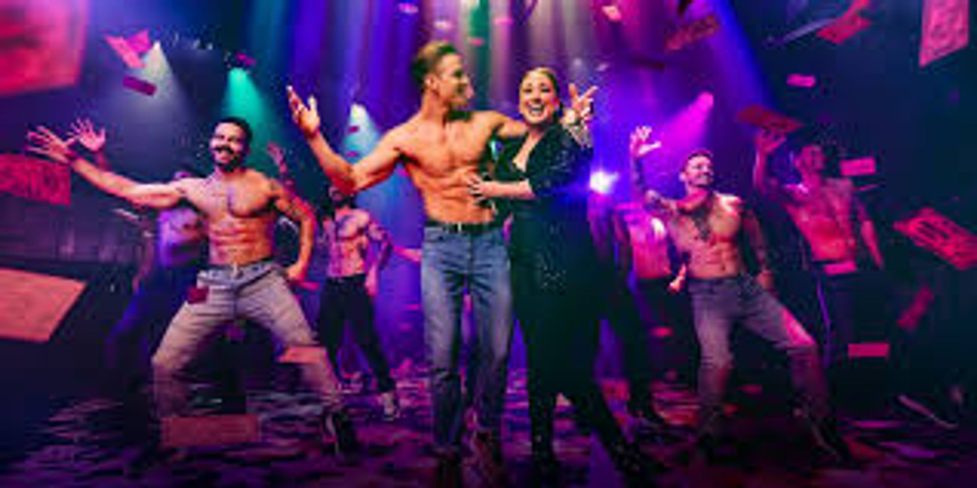 High-energy cabaret stage show with a smiling female lead surrounded by shirtless male dancers, flying paper bills and vivid purple-pink spotlights.