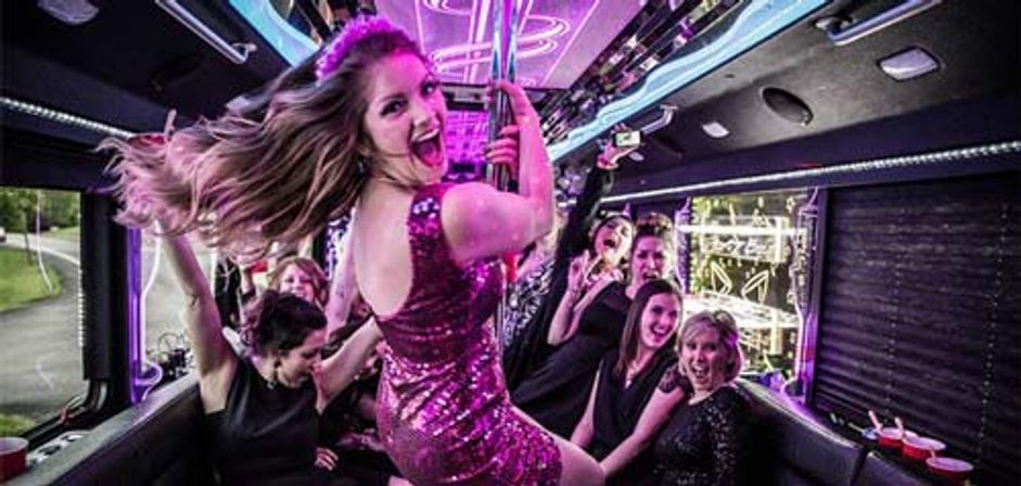 Women celebrating a bachelorette-style party inside a neon-lit party bus, a woman in a pink sequin dress dancing on a pole while friends cheer and laugh.