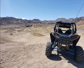 Rear view of an off-road UTV parked on sandy desert dunes with rugged mountains and a clear blue sky
