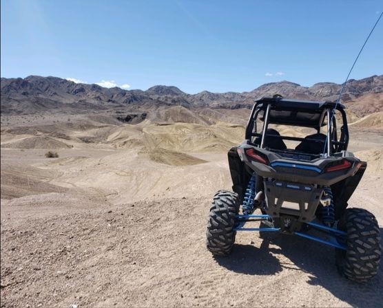 Rear view of an off-road UTV parked on sandy desert dunes with rugged mountains and a clear blue sky
