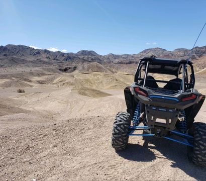 Rear view of an off-road UTV parked on sandy desert dunes with rugged mountains and a clear blue sky