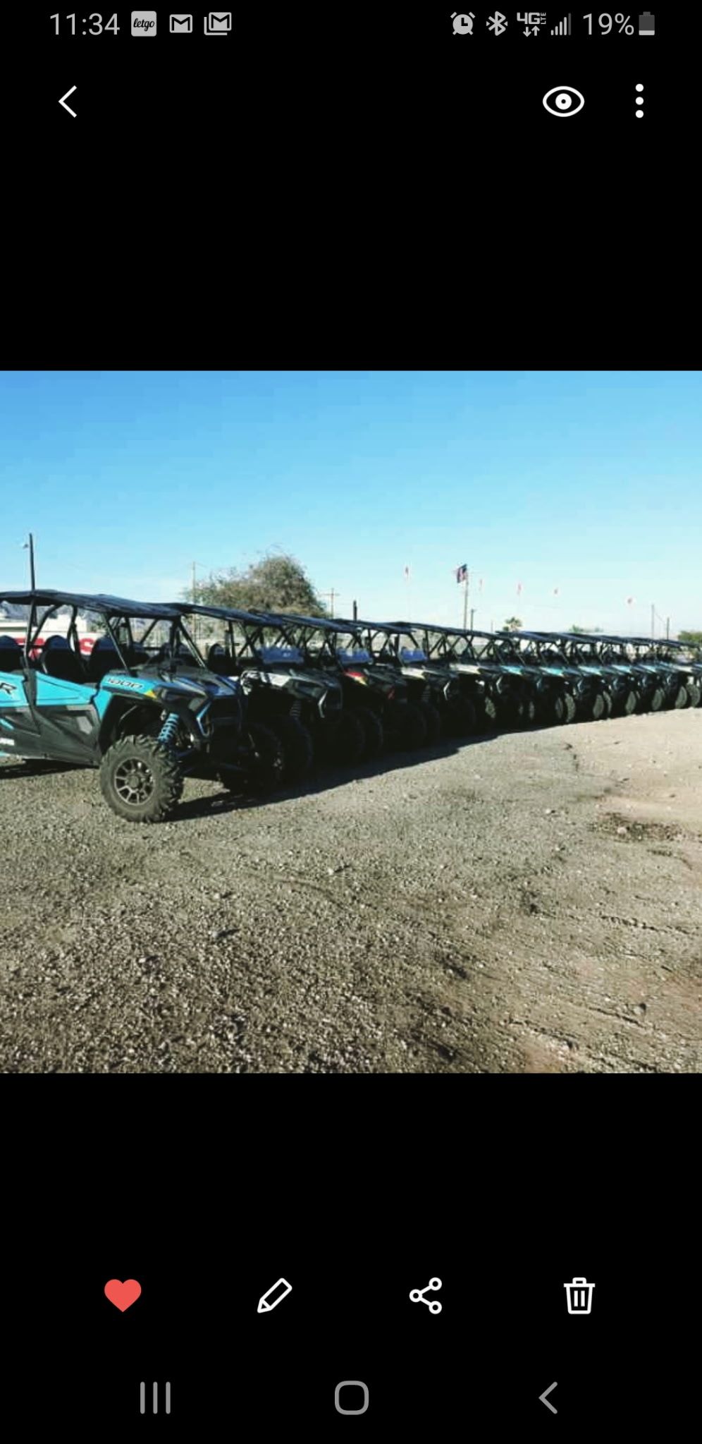 Long row of side-by-side UTVs parked on a gravel lot under a clear blue sky, ready for off-road desert tours